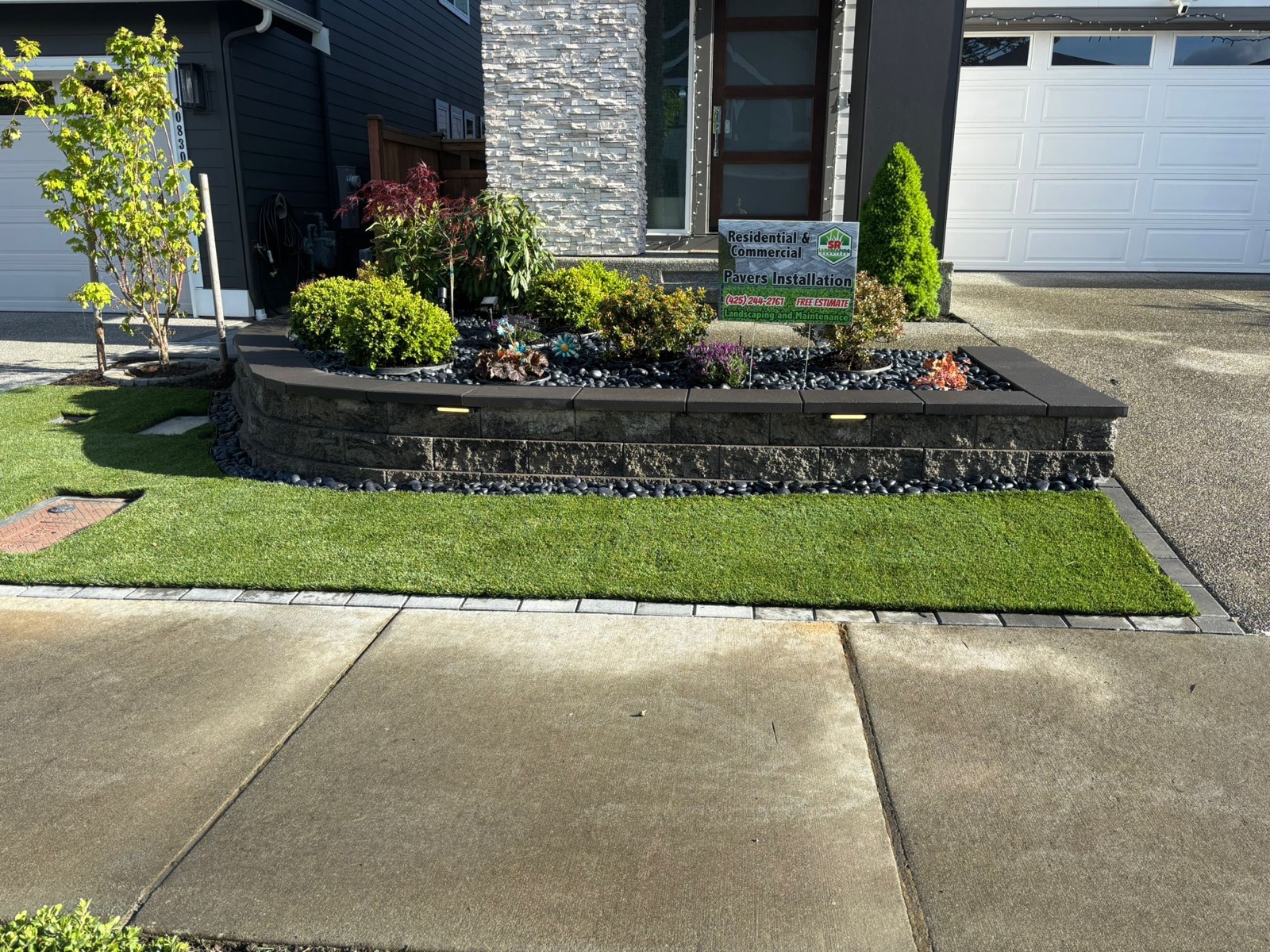 Front yard landscaping with plants, lawn, stone border, and pavers